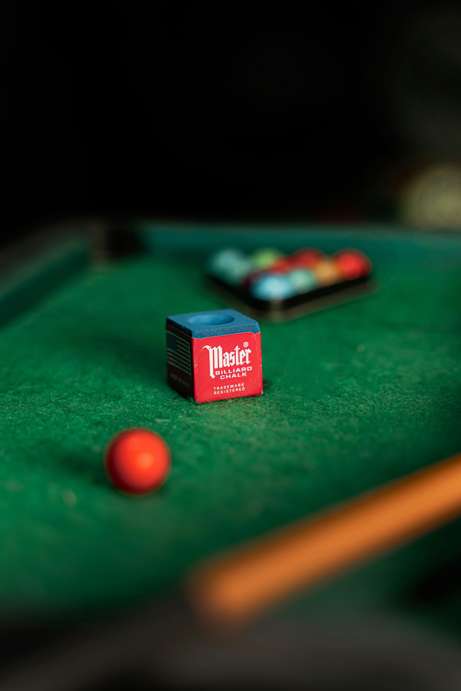 Pool chalk on green felt with billiard balls in the background